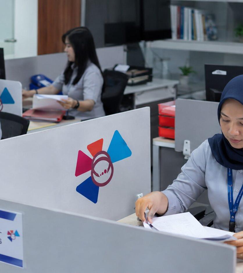 Staf back office SKB memverifikasi dokumen di area kerja kubikel.